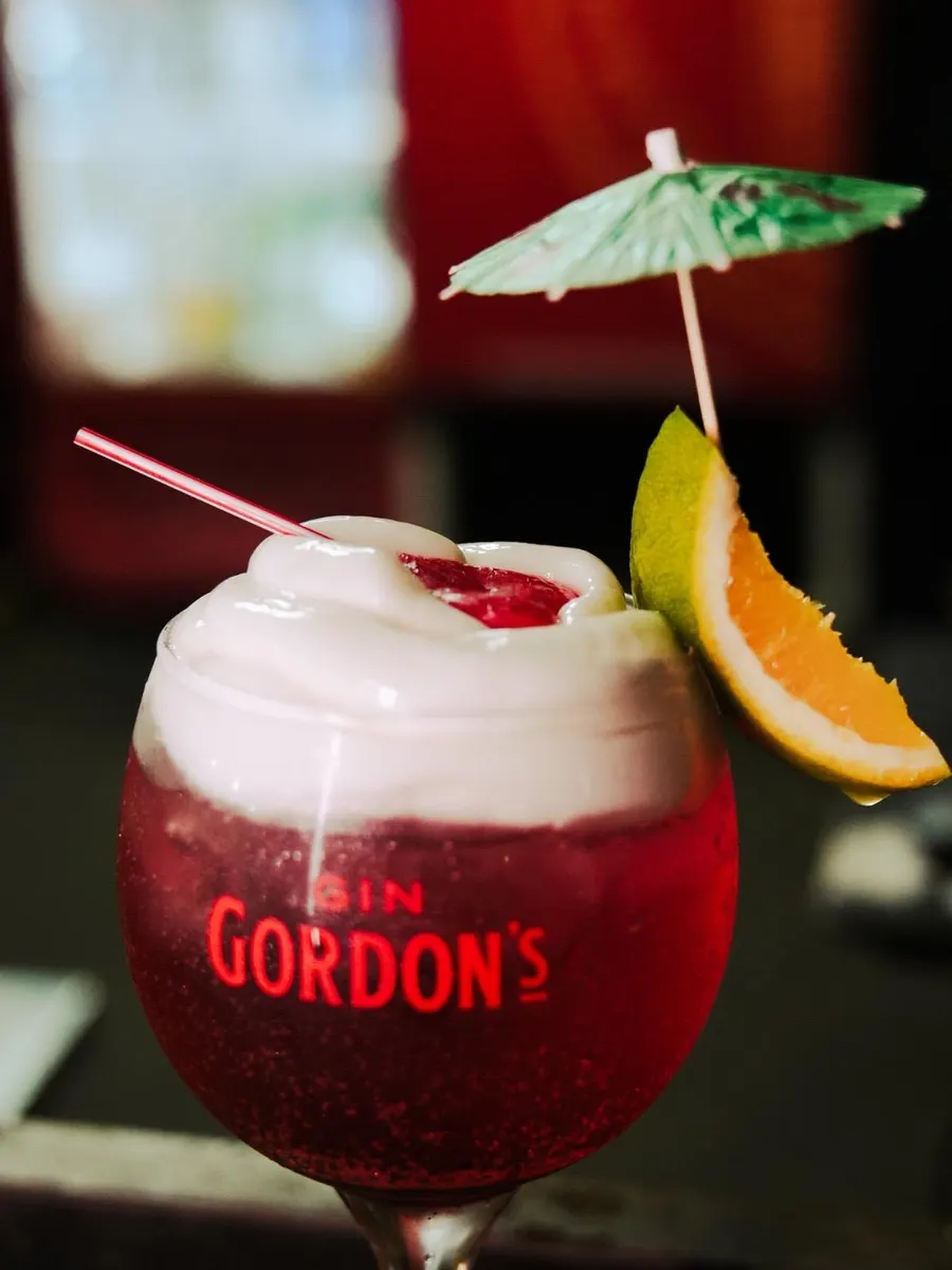 Taça de drink vermelho coberto por espuma de morango, com sombrinha de papel